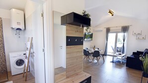 A modern living space with a built-in washer and dryer, a dining area with a table and chairs, and a black sofa. - Modern Holiday Home With Shared Pool (Umag)
