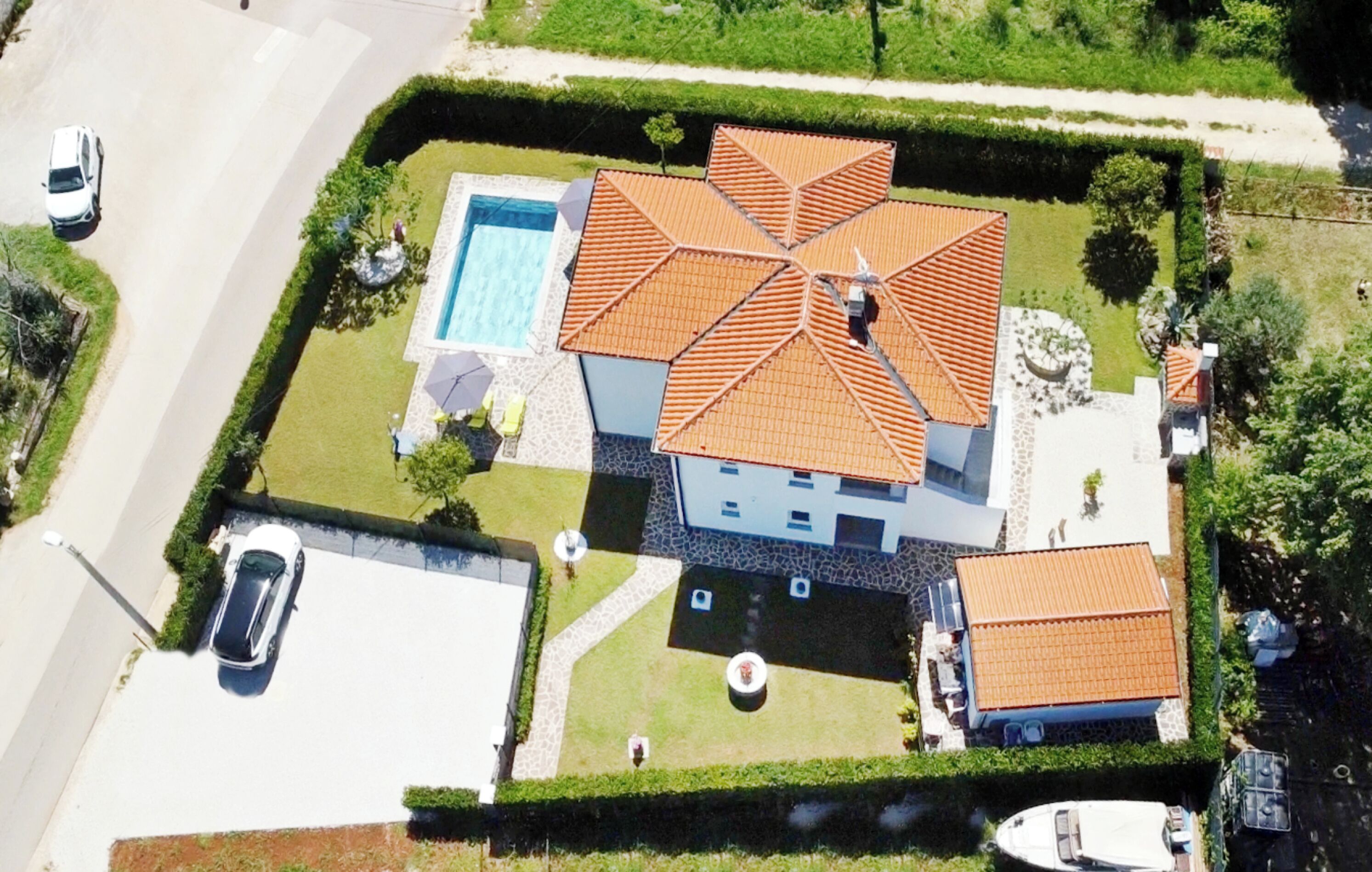 Eine Vogelperspektive auf ein Haus mit Swimmingpool, Ziegeldach und gepflegtem Rasen.