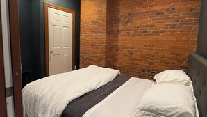 Une chambre avec un lit double, un mur décoratif en briques, une porte en bois et un luminaire au plafond.