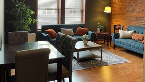 Un salon moderne avec un canapé, une table basse et des fauteuils. On y trouve également une table à manger avec des chaises, une plante en pot et une lampe.