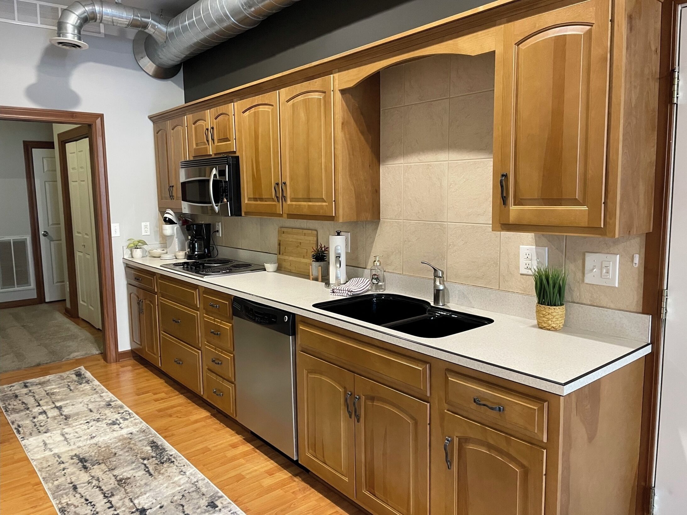 Una cocina moderna con armarios de madera, un lavamanos de acero inoxidable y un microondas integrado.