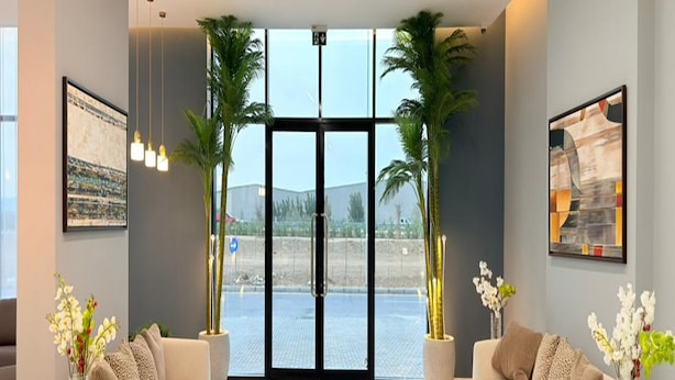 A modern living room with two sofas, a coffee table, and a large window with a view of a parking lot. - Luxury Apartment with Pool Gym & Free Parking at Equiti Gates Jebel Ali (Dubai)