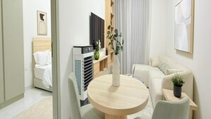 A modern, well-lit room with a round wooden table, two chairs, a sofa, a TV, and a potted plant. - Luxury Apartment with Pool Gym & Free Parking at Equiti Gates Jebel Ali (Dubai)
