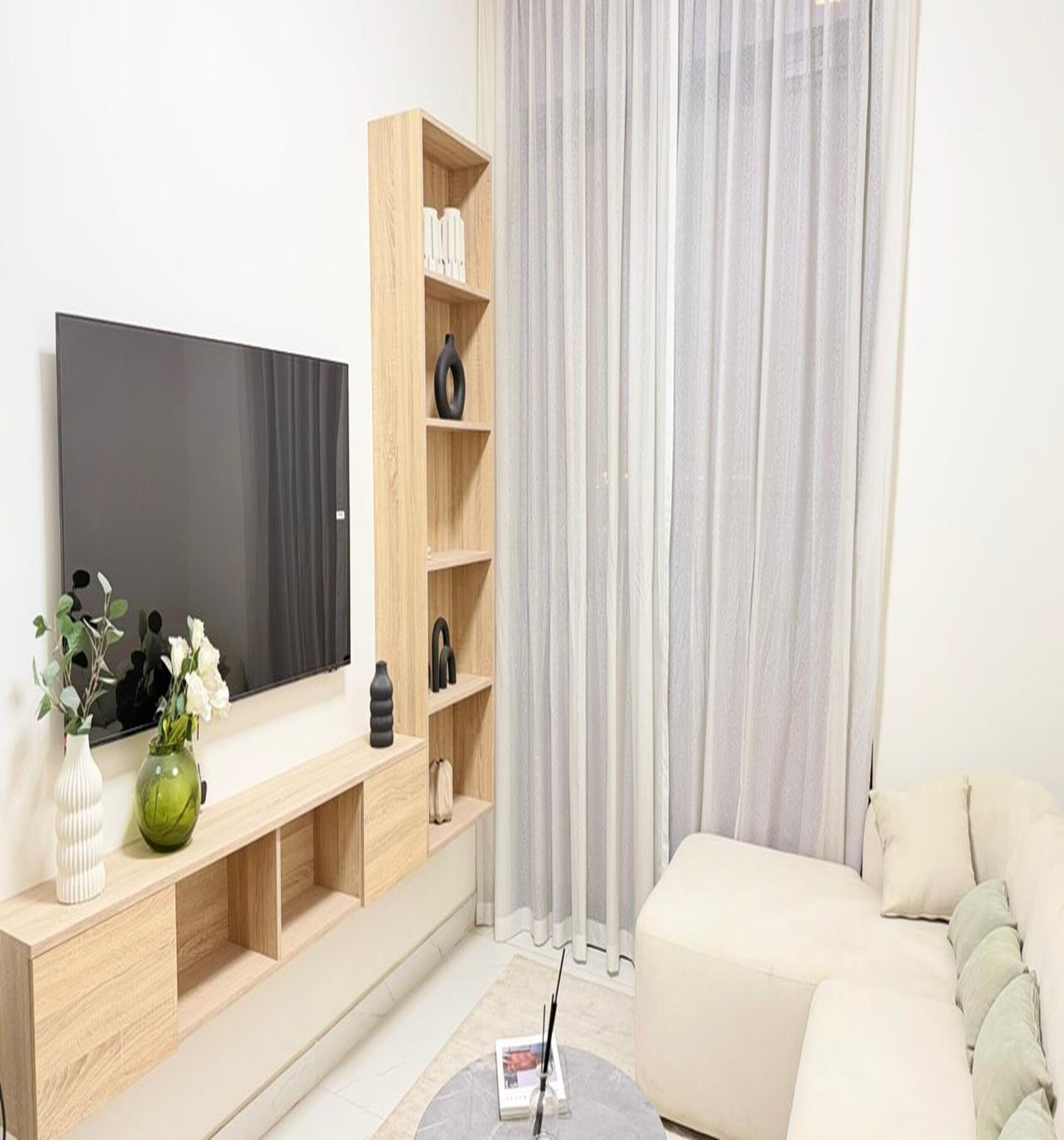 Ein modernes Wohnzimmer mit Flachbildfernseher, Holzbögen, einer grünen Vase und einem beigefarbenen Sofa.