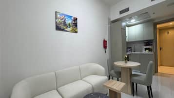 A modern living room with a sofa, a round table, and a small coffee table. There is a painting on the wall and a kitchen area in the background.