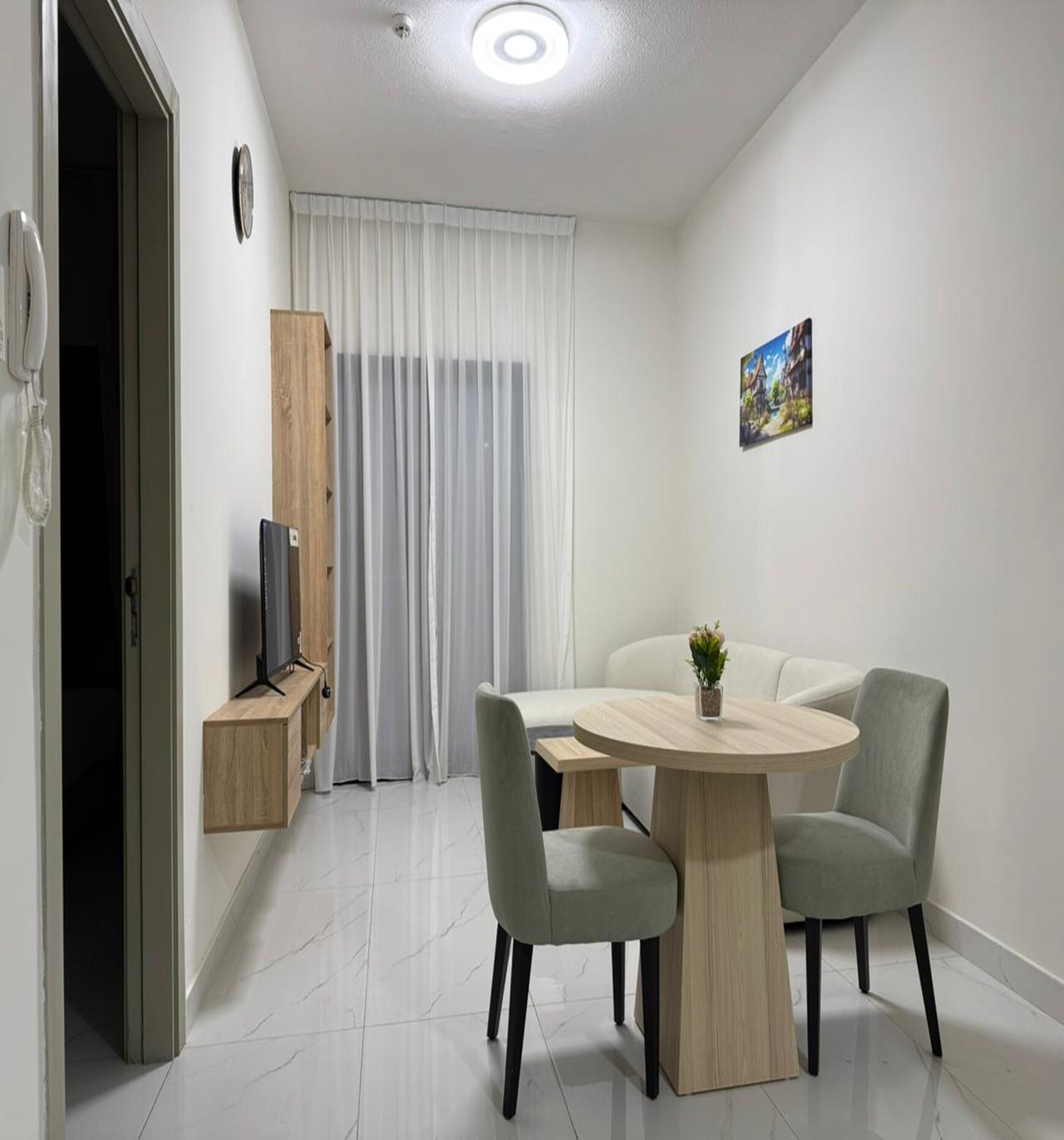 A modern, well-lit room with a dining table, two chairs, a small plant, and a painting on the wall.
