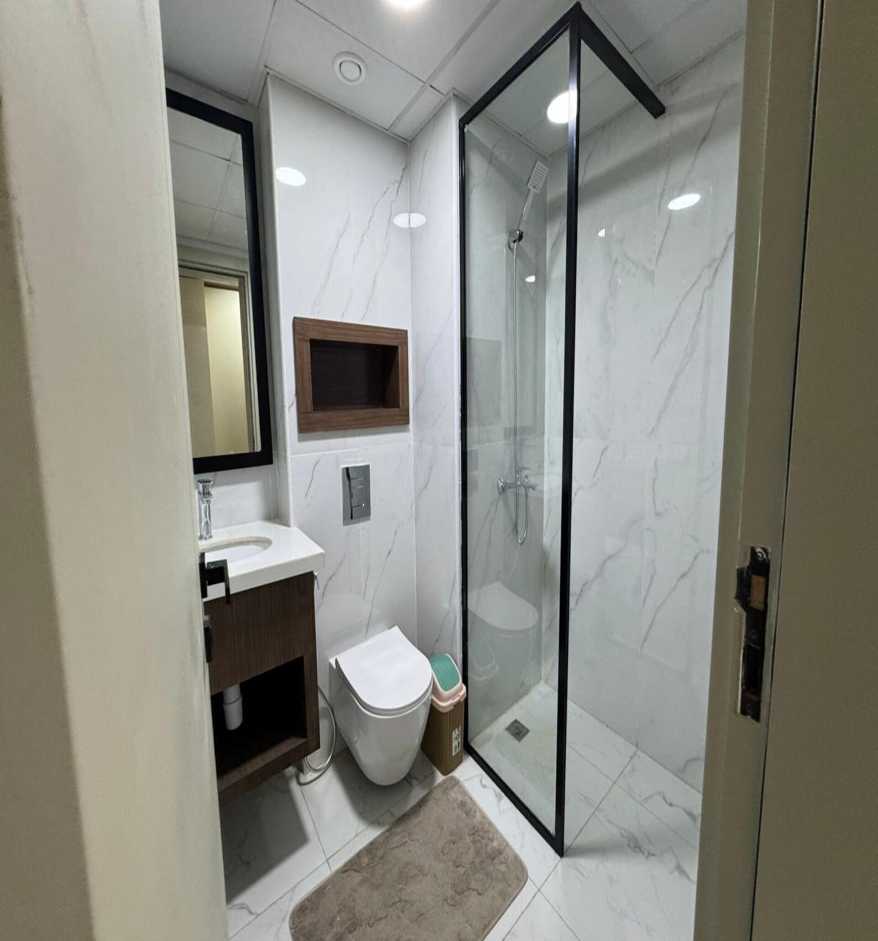 Um banheiro moderno com box de vidro, vaso sanitário e pia com bancada de madeira.