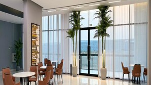 A modern hotel lobby with a large open space, multiple seating areas, and large windows offering a view of the sea. - Luxury Apartment with Pool Gym & Free Parking at Equiti Gates Jebel Ali (Dubai)