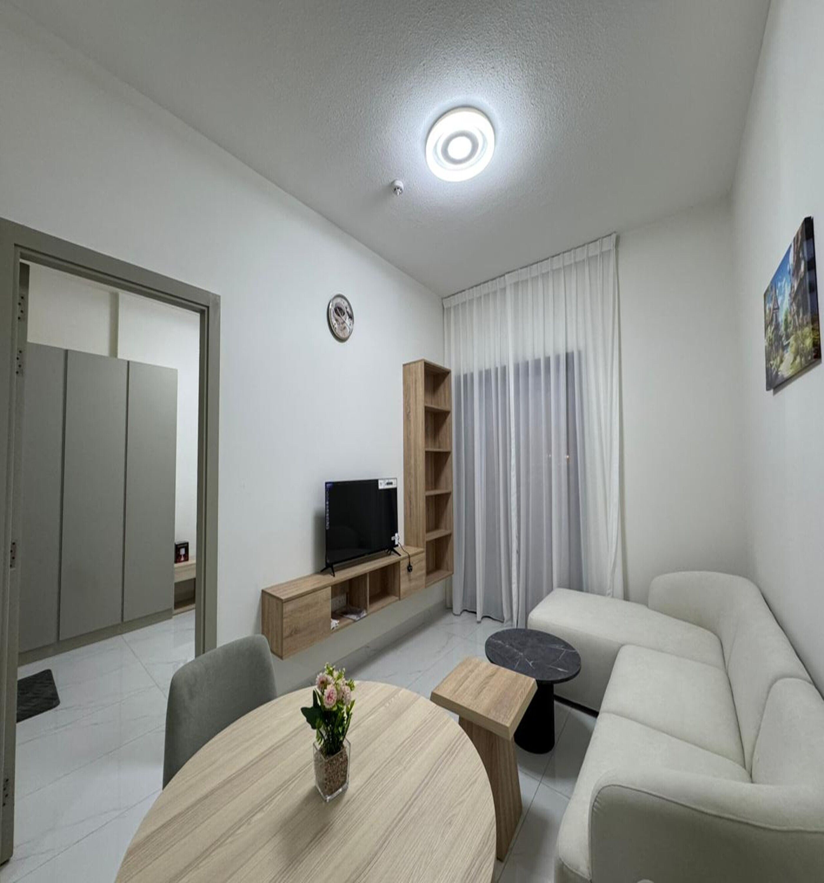 Una sala de estar moderna con un sofá, un televisor sobre un mueble de madera, una mesita y una planta decorativa.