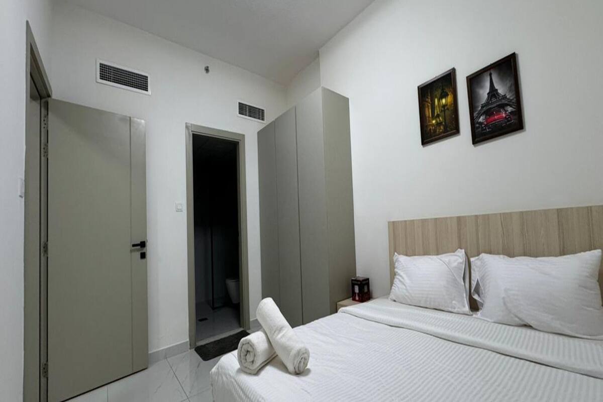 A hotel room with a bed, two paintings, a nightstand, and a door leading to a bathroom.