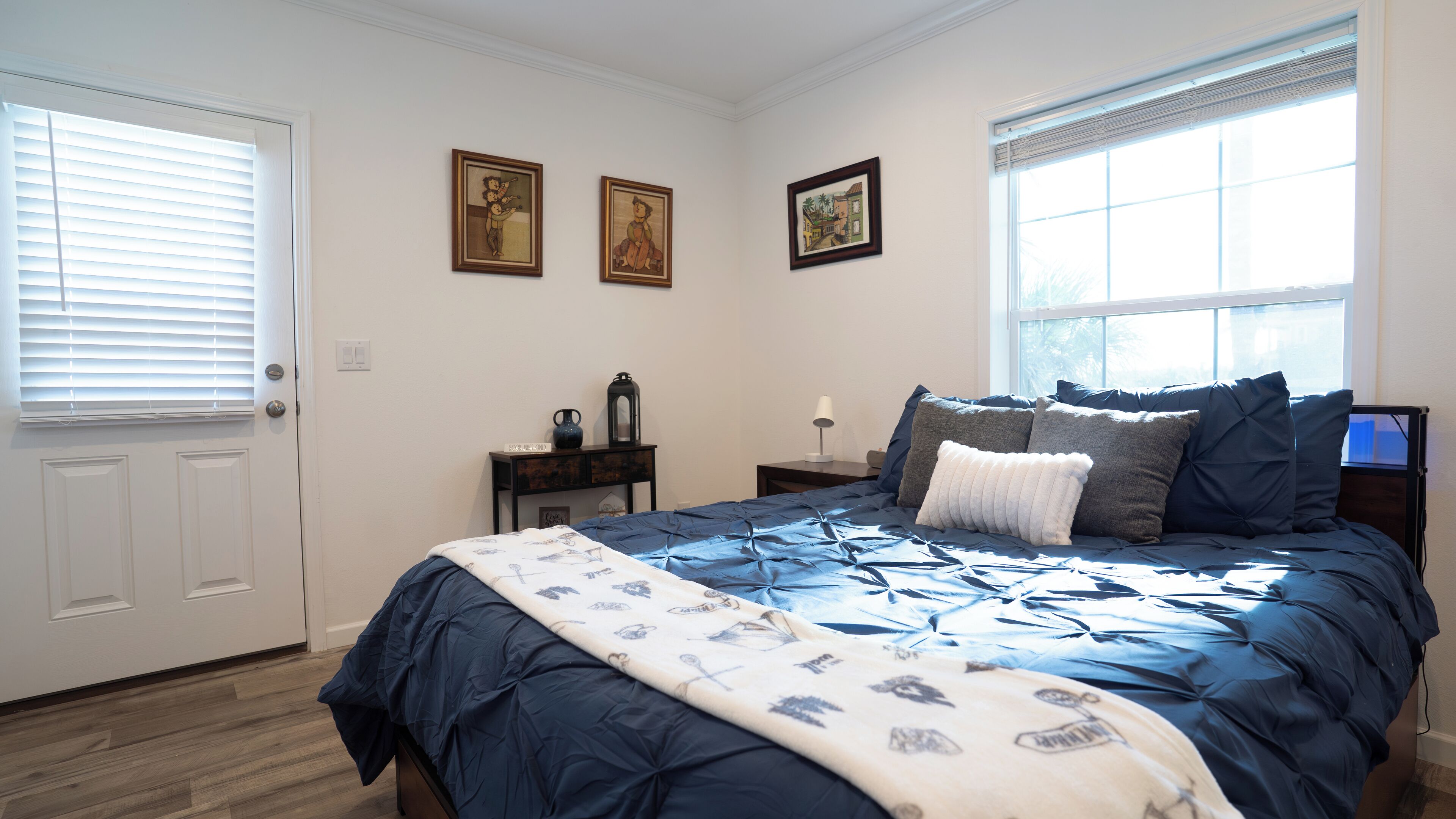 A bedroom with a bed, a nightstand, a dresser, and three framed pictures on the wall.