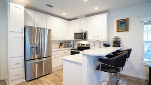 A modern kitchen with white cabinets, stainless steel appliances, and a bar area with black stools. - Charming 1/1 home across the street from the ocean sunsets, dock space included! (Bonita Springs)