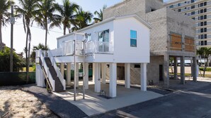 A two-story house with a balcony, a staircase, and a view of a palm tree. - Charming 1/1 home across the street from the ocean sunsets, dock space included! (Bonita Springs)