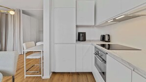 Een compacte keuken met witte kastjes, een ingebouwde oven en een koffiezetapparaat op het aanrecht.