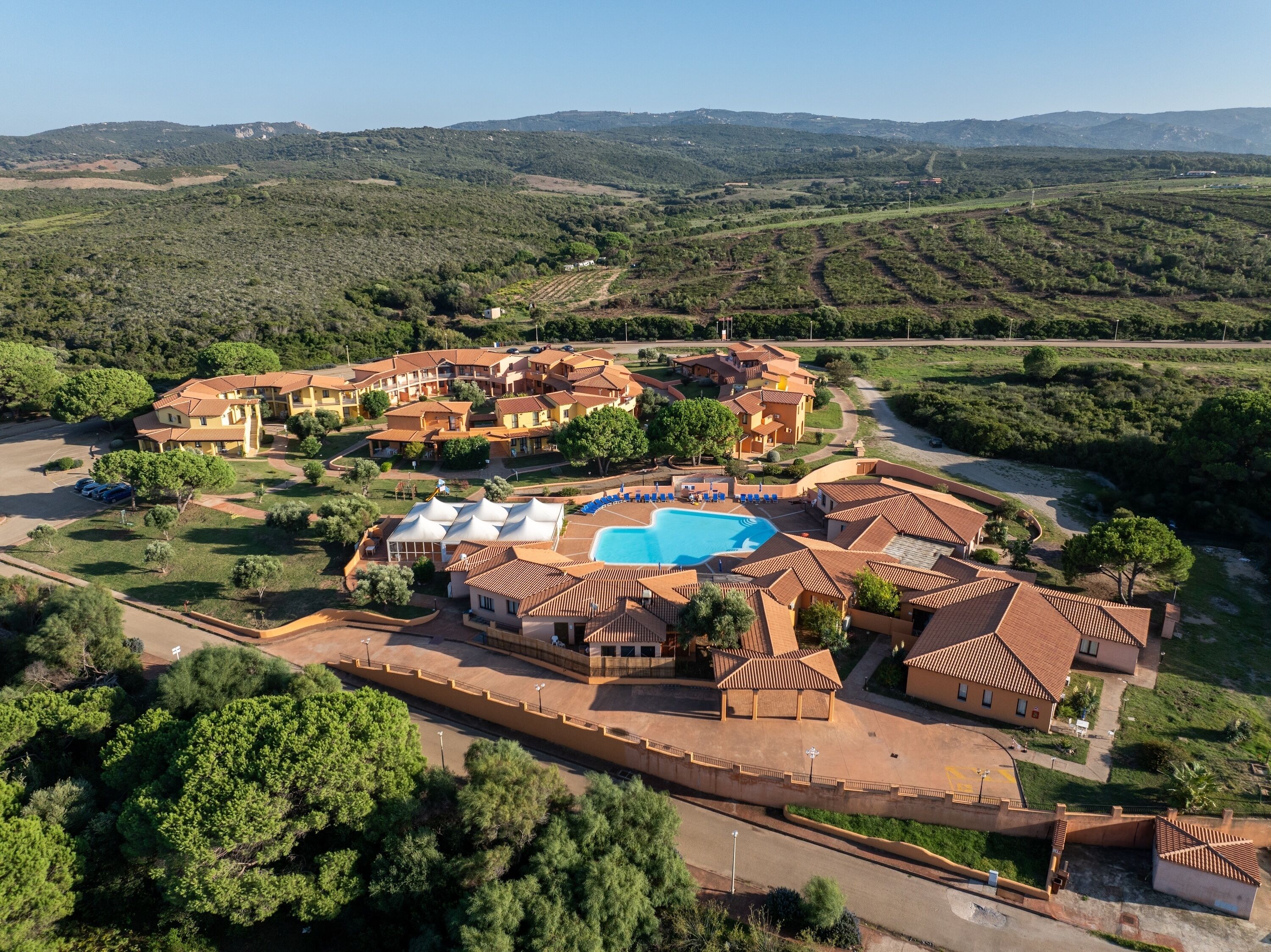 An aerial view of a resort with multiple buildings, a swimming pool, and surrounding greenery.