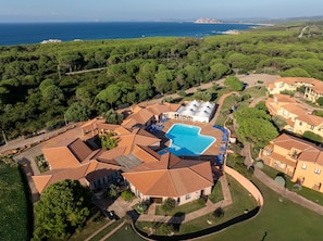 An aerial view of a resort with a swimming pool surrounded by villas, a clear view of the sea, and a lush green landscape. - Cozy Accommodation With Shared Pool (Aglientu)
