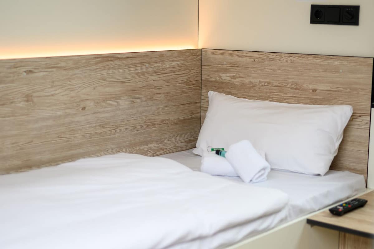 A neatly made bed with white linens and pillows, a remote control on the side table, and a wooden headboard.