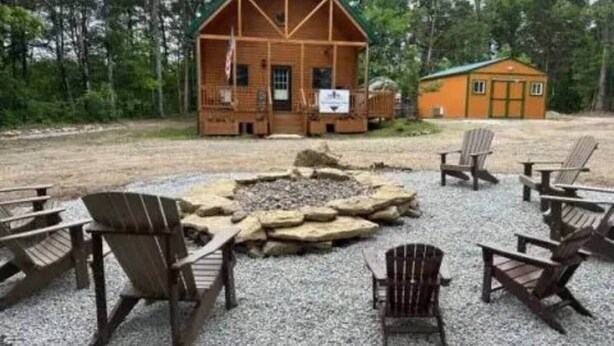 Eine Hütte mit Feuerstelle und Adirondack-Stühlen davor.