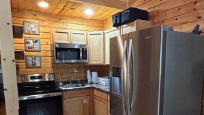 Eine kleine Küche mit Holzwänden, einem Edelstahlkühlschrank, einer Mikrowelle und einem Backofen.