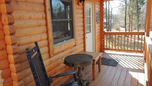 A log cabin with a wooden porch, a table, and a chair. - Justin Fitch Cabin - Active Heroes (Bullitt County)