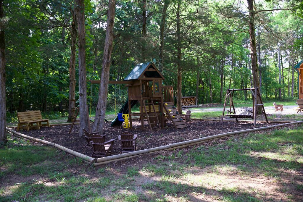 Una estructura de madera para jugar con tobogán y columpio en un parque arbolado.