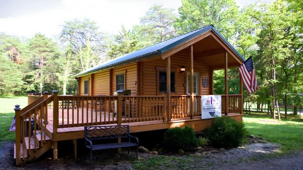 A wooden cabin with a porch, an American flag, and a sign that reads "The Julia Fish Cabin." - Justin Fitch Cabin - Active Heroes (Bullitt County)