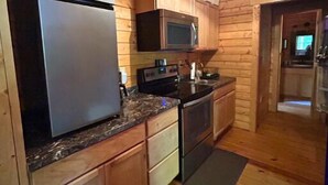 A compact kitchen with wooden walls, a refrigerator, microwave, stove, and granite countertop. - Justin Fitch Cabin - Active Heroes (Bullitt County)