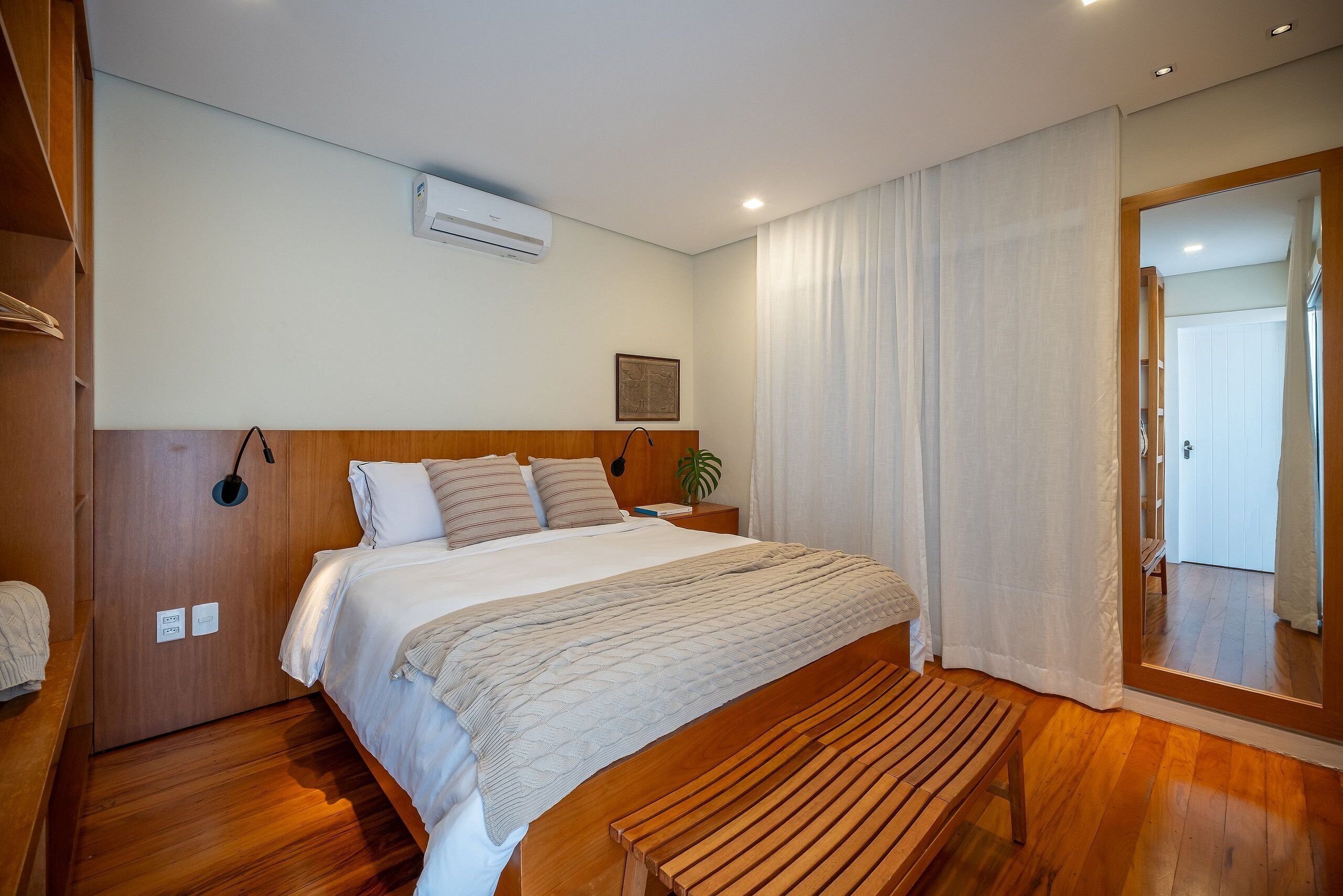 A bedroom with a wooden bed, a bedside table, a bench, and a large mirror.