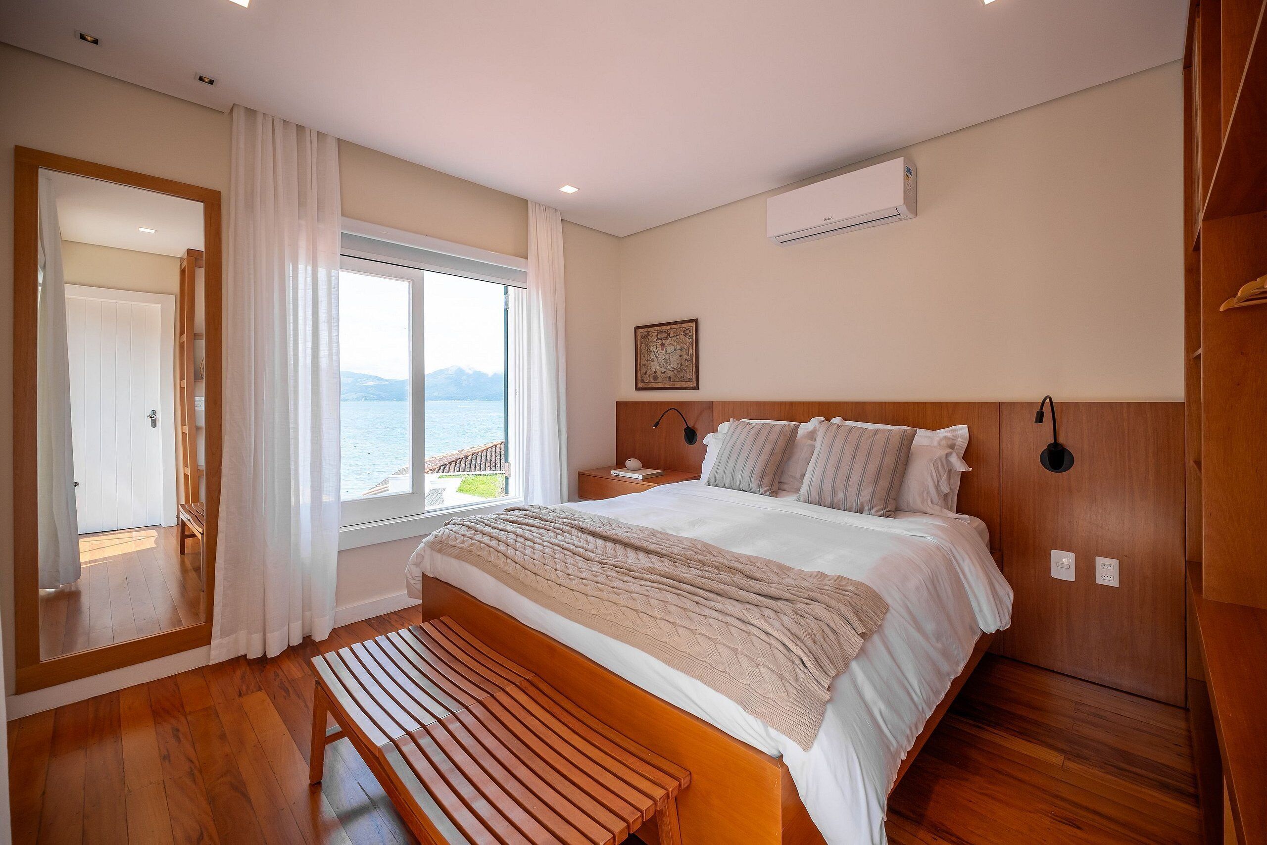 Ein Schlafzimmer mit einem großen Bett, Holzboden, einer Bank, einem Fenster mit Aussicht und einer Klimaanlage.