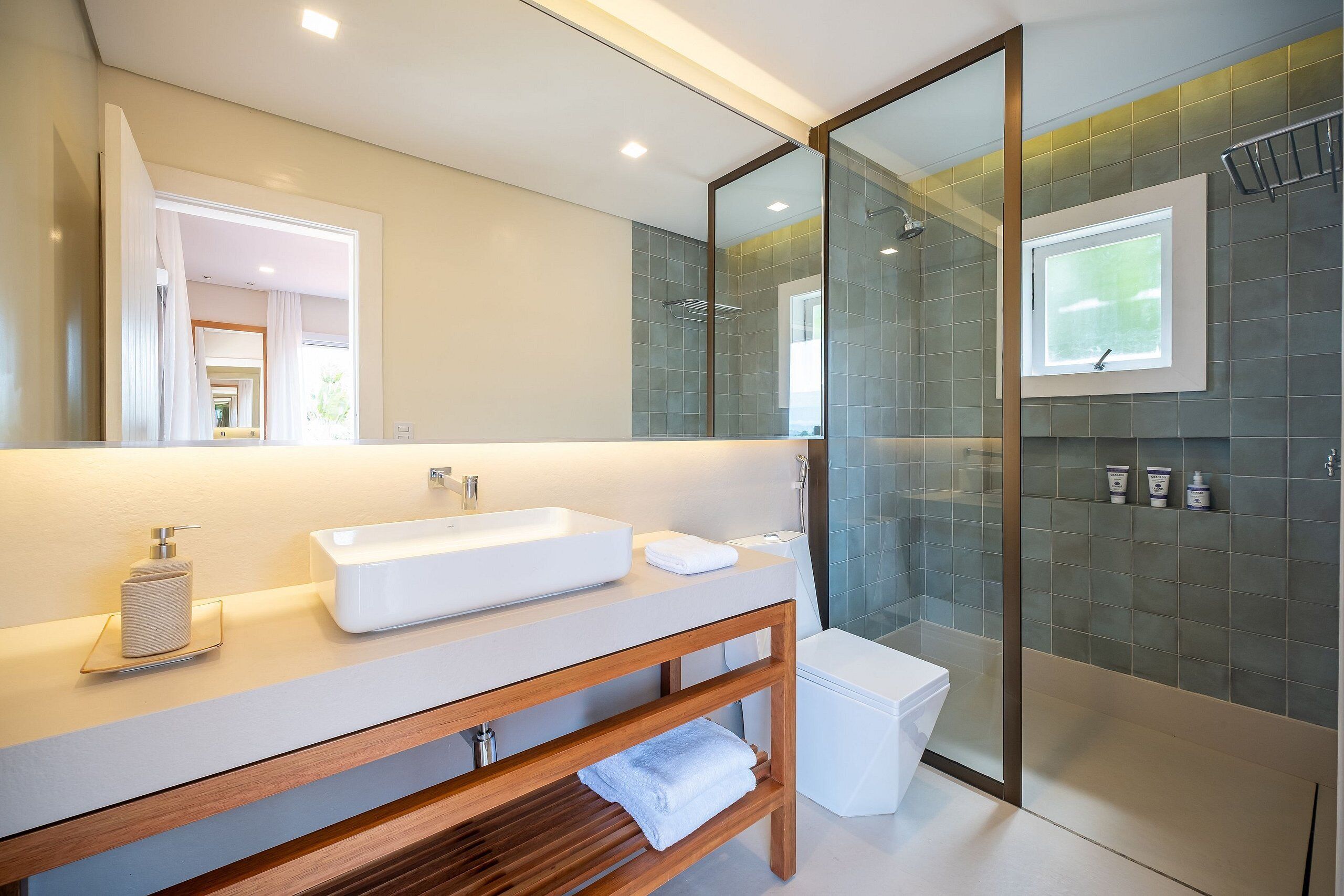 Un baño moderno con un espejo grande, un lavabo blanco, una cabina de ducha de vidrio y un mueble de tocador de madera.