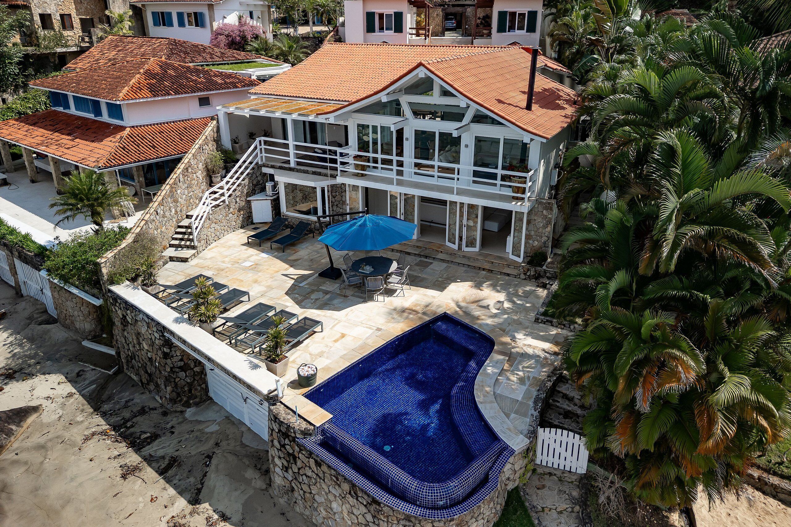 A two-story house with a swimming pool, stone walls, and a patio area.