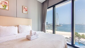 A hotel room with a large bed, a view of a coastal area, and a Ferris wheel in the distance. - Full Sea View!, 2br in JBR (Dubai)