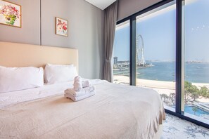 Ein Hotelzimmer mit einem großen Bett, Blick auf eine Küstenlandschaft und einem Riesenrad in der Ferne.