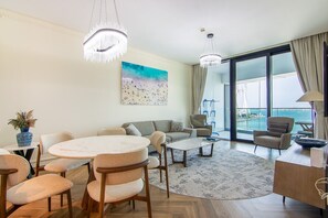 Ein modernes Wohnzimmer mit einem runden Esstisch, Sofas und Meerblick durch große Fenster.