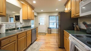 A modern kitchen with wooden cabinets, stainless steel appliances, and a large window. - Spacious 4BR Retreat w/Free Tix | Fire Pit + Grill (Asheville)