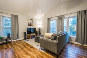 Ein Wohnzimmer mit grauem Sofa, Fernseher und Holzboden.