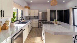 A modern kitchen with white cabinets, stainless steel appliances, a marble countertop, and a large window. - Bay View Home with Rooftop & Private Pool (El Centenario)
