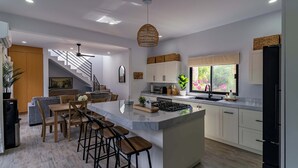 A modern kitchen with a central island, bar stools, a microwave, and a window with a view of greenery. - Bay View Home with Rooftop & Private Pool (El Centenario)