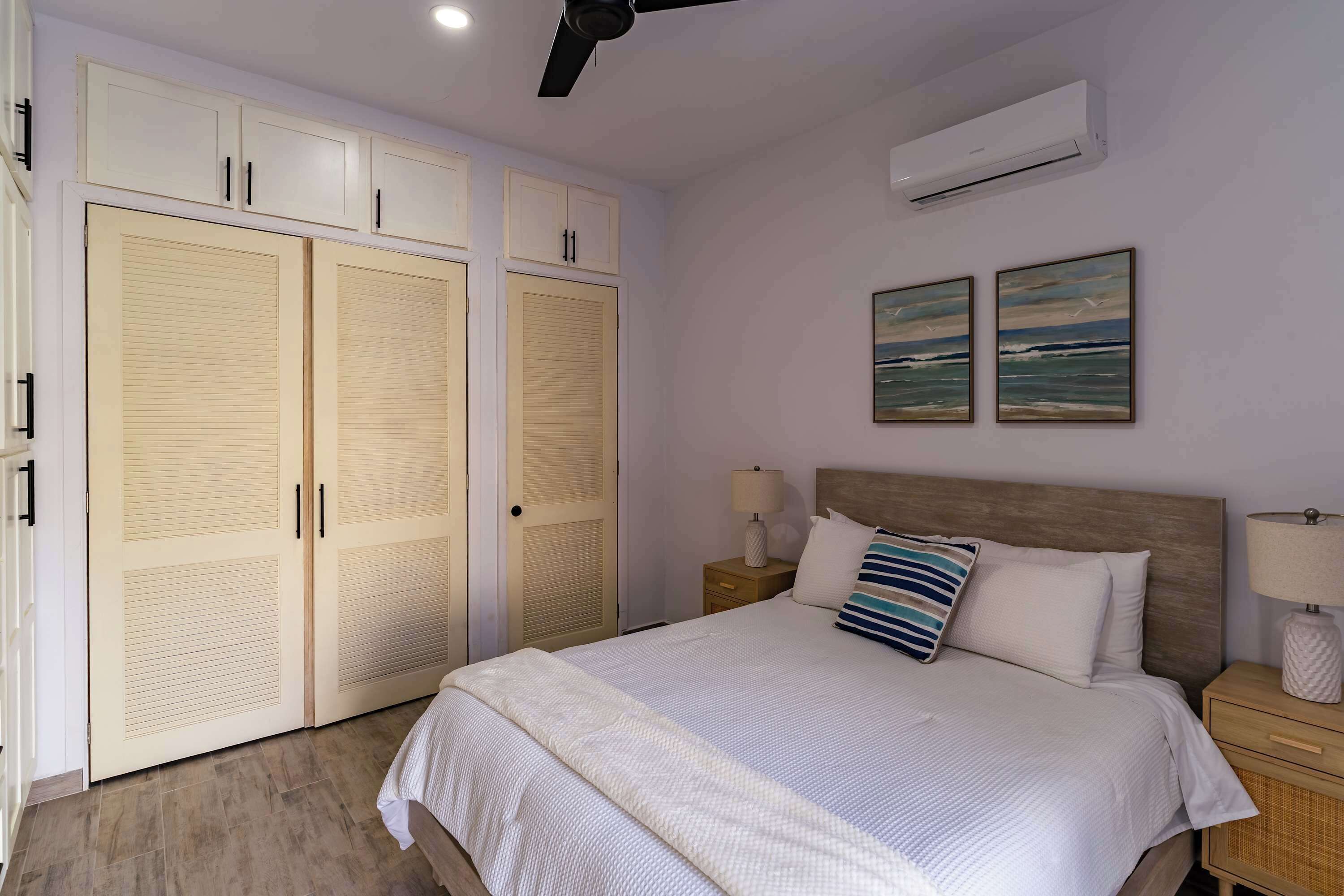 A bedroom with a bed, nightstands, a ceiling fan, an air conditioner, and a wardrobe.
