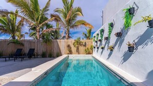 A swimming pool with a tiled edge, surrounded by lounge chairs and palm trees. - Bay View Home with Rooftop & Private Pool (El Centenario)