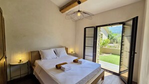 Ein Schlafzimmer mit Bett, Nachttischlampen und Blick auf einen Garten durch eine offene Tür.