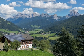 Eine Berglandschaft mit einem Haus, das mit Solaranlagen ausgestattet ist, umgeben von grünen Feldern und bewaldeten Hügeln.
