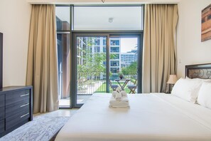 A hotel room with a large bed, a desk, and a view of a building and greenery outside. - Charming 1br in Dubai Hills (Dubai)