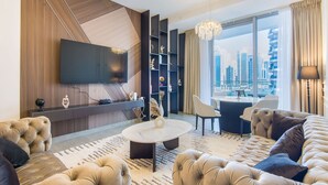A modern living room with a flat-screen TV, a sofa, a coffee table, and a city view through large windows. - Marina View- 1br in Stella Maris (Dubai)
