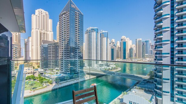 A balcony with a view of a cityscape, a river, and a wooden bench. - Marina View- 1br in Stella Maris (Dubai)