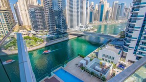 A high-rise building with a rooftop pool, a marina with boats, and a river in the background. - Marina View- 1br in Stella Maris (Dubai)