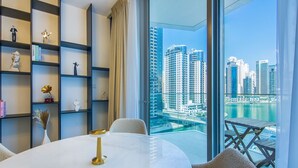 A modern living room with a round table, a bookshelf, and a view of a cityscape and water. - Marina View- 1br in Stella Maris (Dubai)