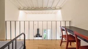 A room with a wooden floor, a black table with red chairs, a white ceiling with exposed beams, and a view through a window to the outside. - Orcagna by MMega (Florence)