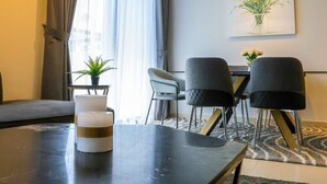 A modern hotel room with a dining area featuring a black table, two black chairs, a small potted plant, and a framed artwork on the wall. - 4BR + Maids Villa in Maple 2, Dubai Hills (Dubai)