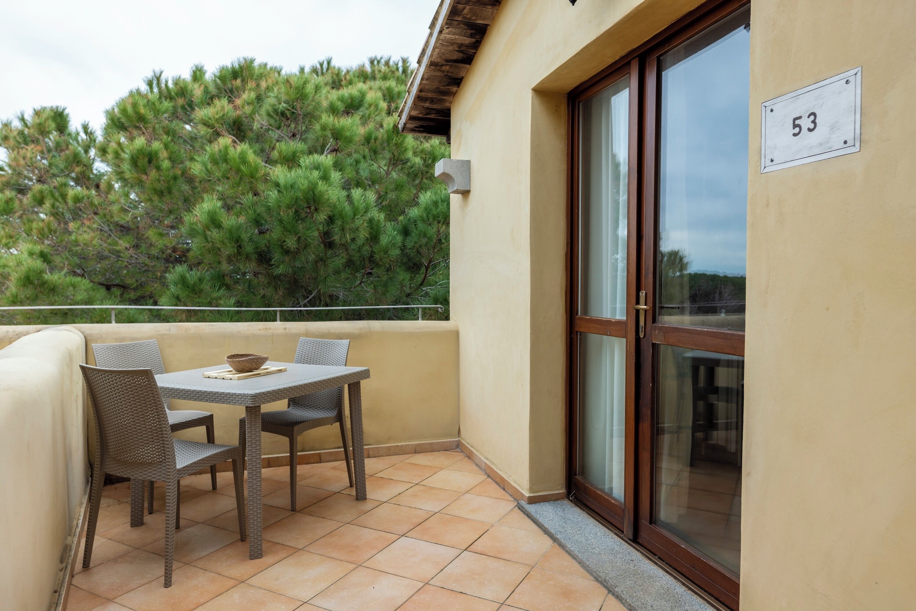 Un balcone con tavolo e sedie, una porta vetrata scorrevole e un cartello con il numero 53 al muro.